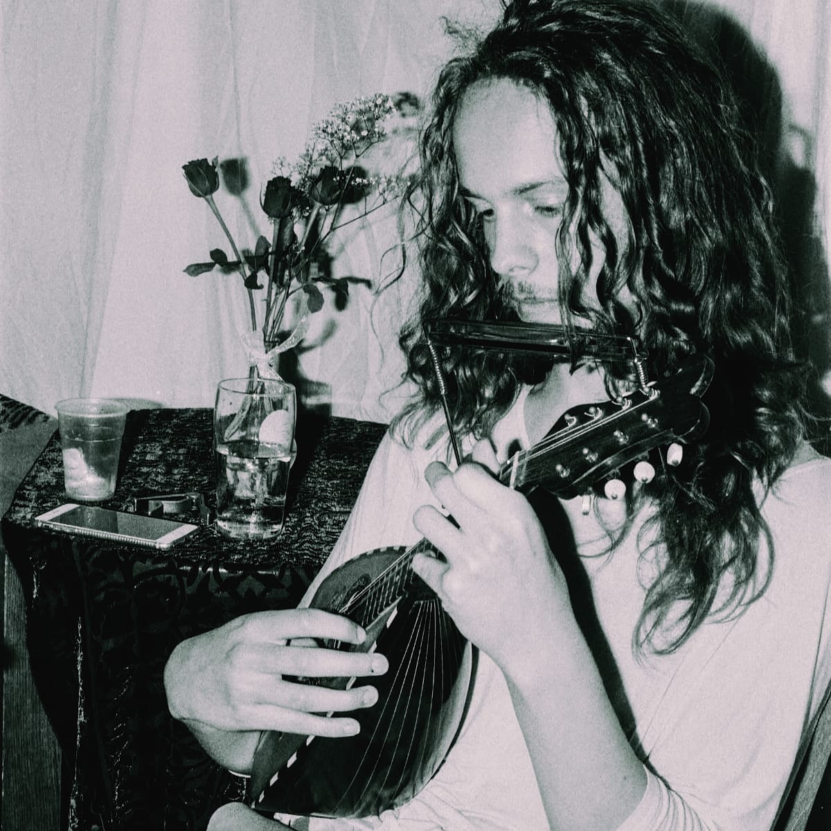 Black and white photo of Louis Gardner at home playing a small lute-like instrument. Photo by Veronica Maier.