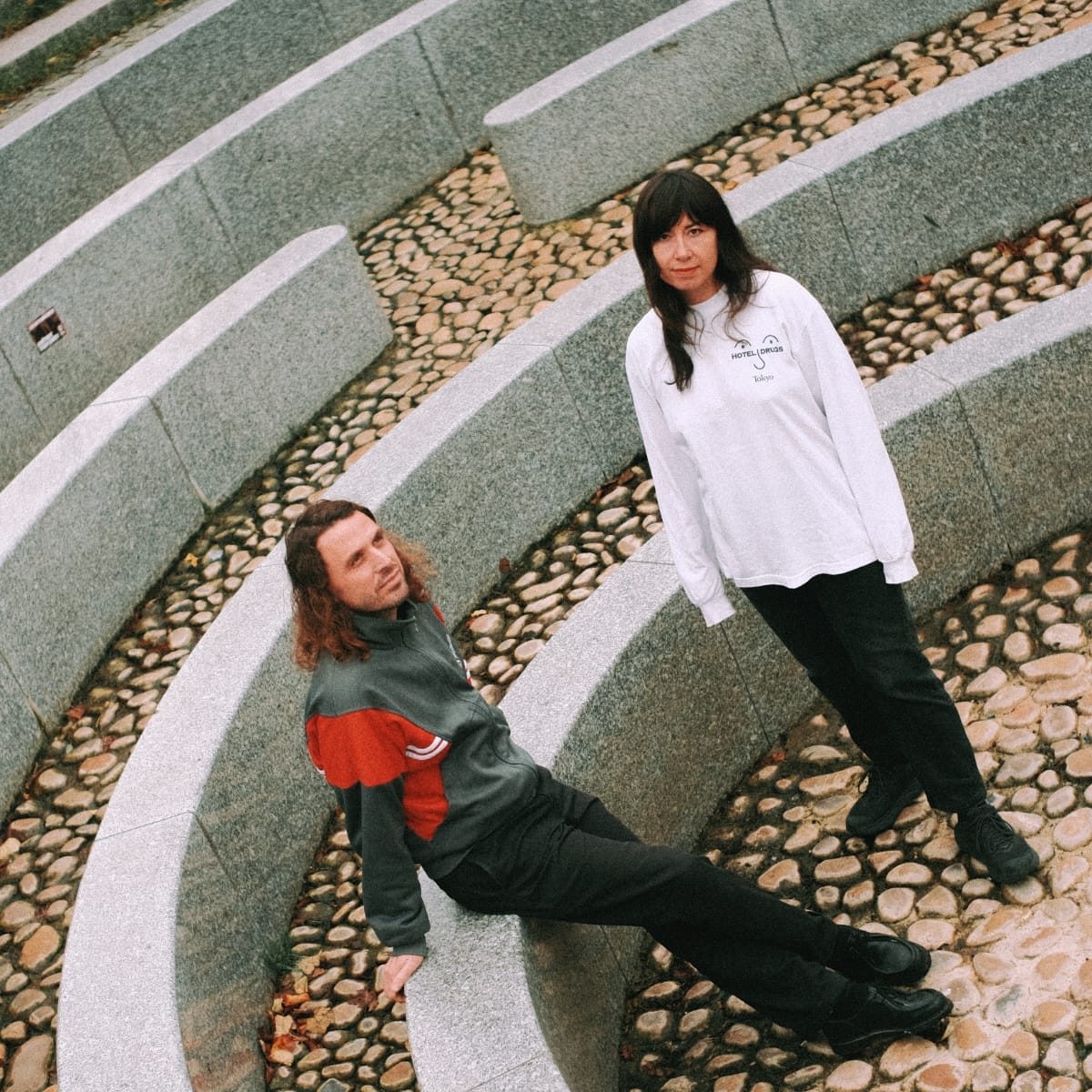 Two members of Special Friend on paved steps with pebble sections, one seated in colorful jacket, one standing in white shirt.