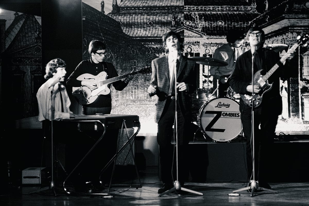 The Zombies perform in vintage black and white photo, ornate backdrop visible, Ludwig drum kit with band name prominent.