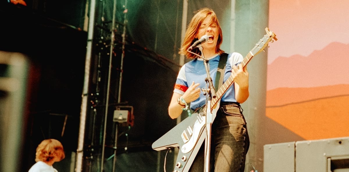 Julia Steiner of Ratboys performs with white electric guitar, singing passionately on stage with warm orange lighting.Photo by Miles Kalchik.