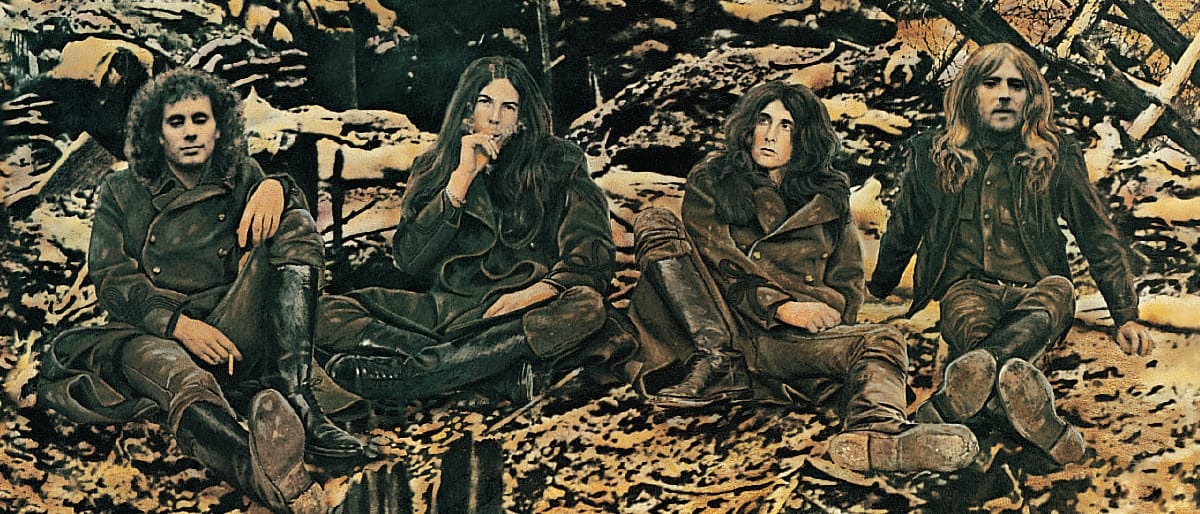 Four members of Armageddon seated on rocky debris in earth-toned vintage photo, wearing leather jackets and boots in casual 1970s style.