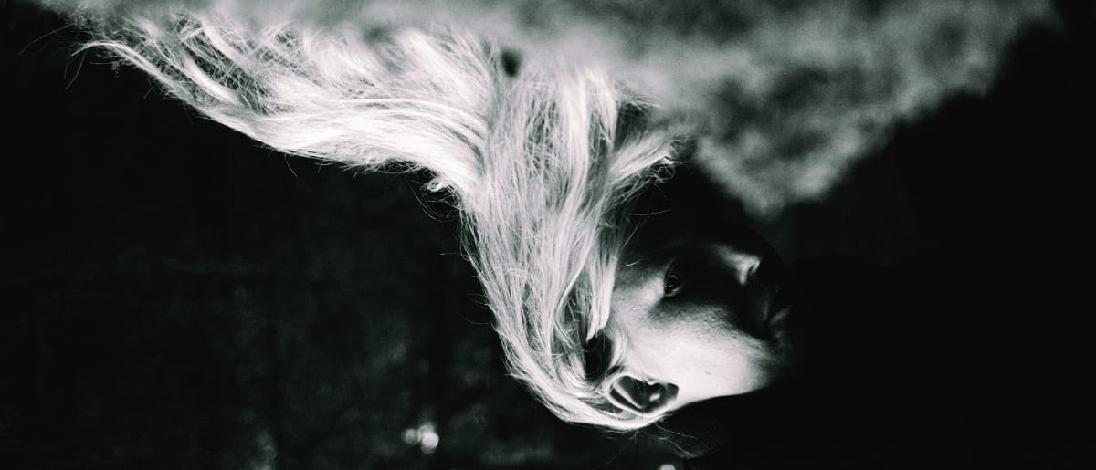 Fågelle photographed from above in black and white, hair spreading dramatically against dark background. Photo by Klara Andersson.