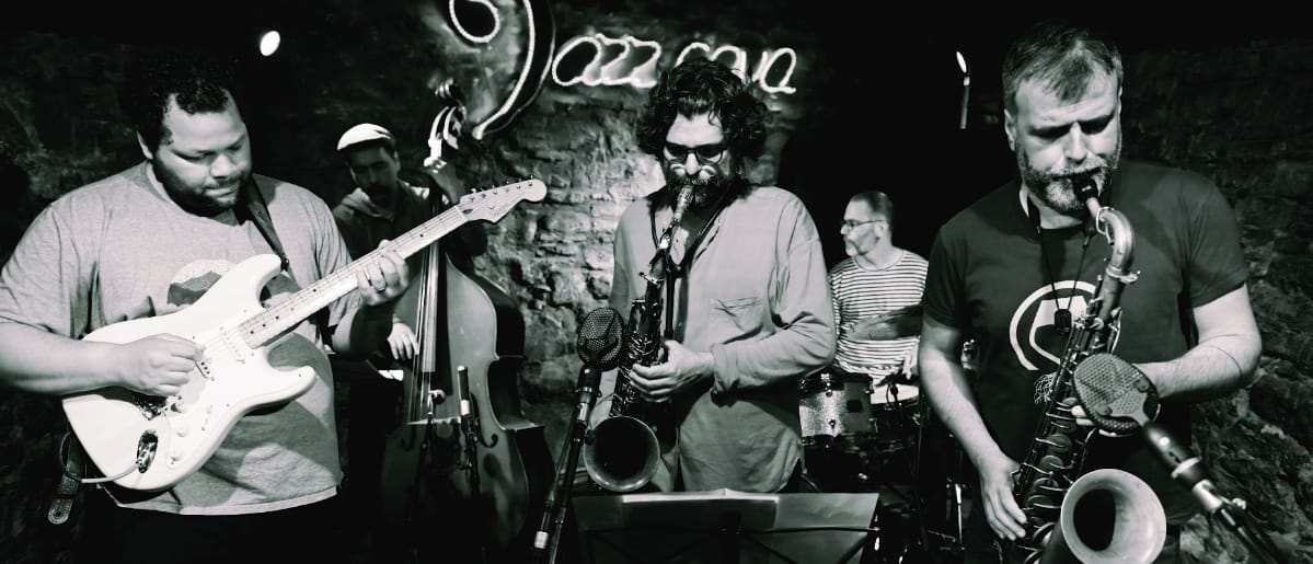 Juanma Trujillo on guitar with band in black and white jazz club performance, saxophone and other musicians visible. Photo by Joan Cortès.