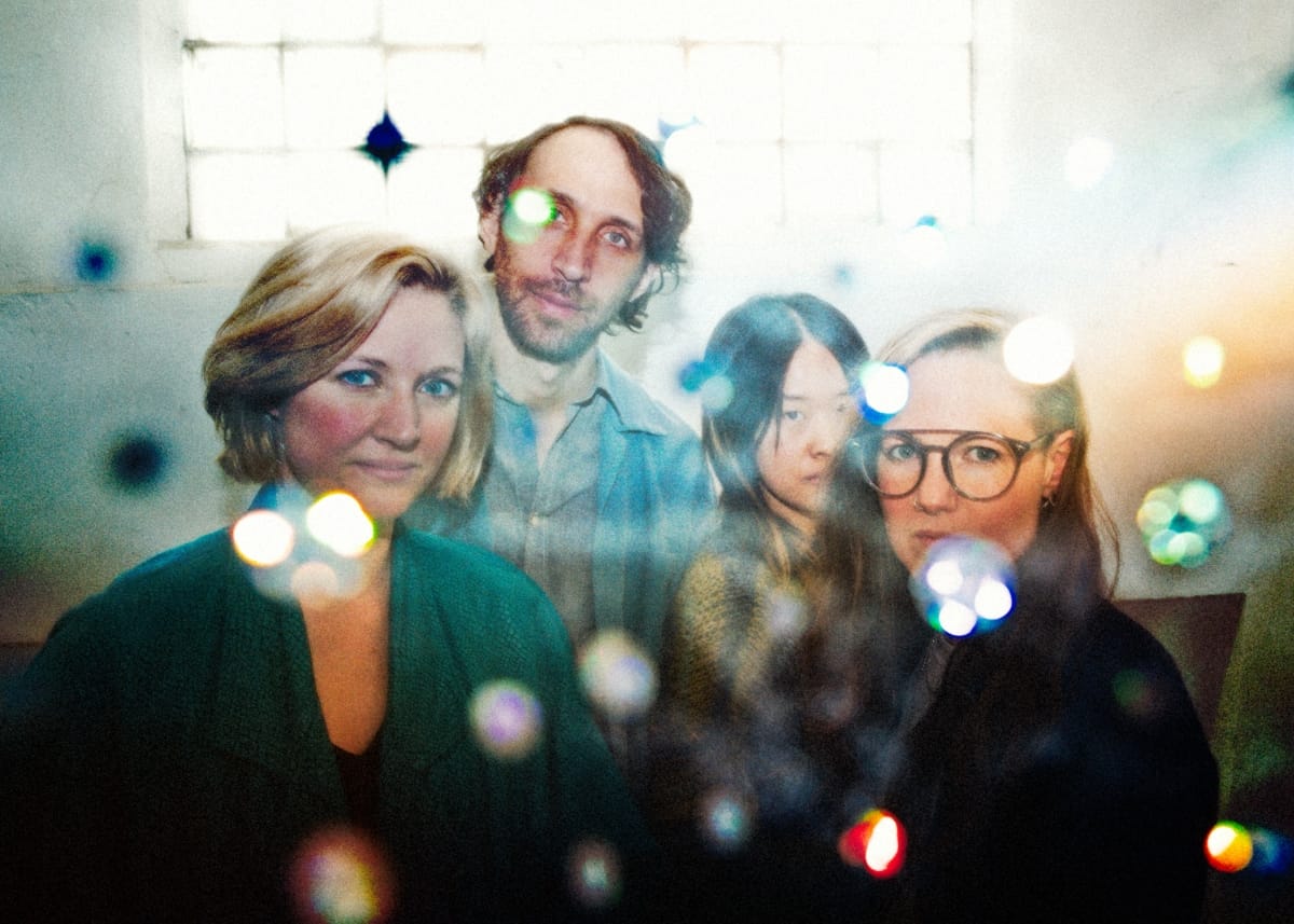 Four members of Bellbird with colorful bokeh light effects in foreground, bright windows behind, soft focus. Photo by Marc Etienne Mongrain.