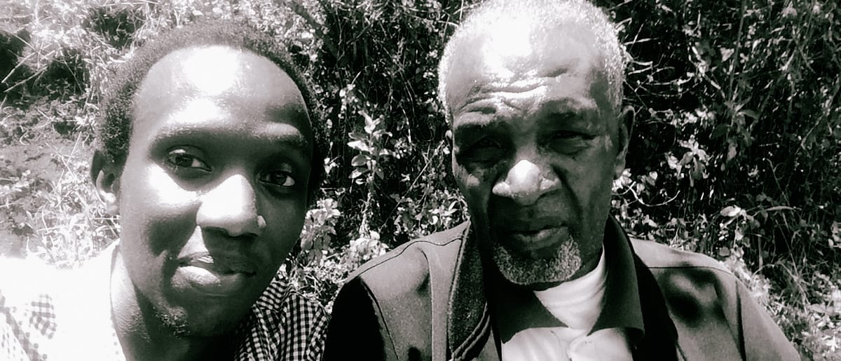 KMRU and Joseph Kamaru pose together outdoors in black and white, with lush foliage behind them. Photo courtesy of Estate of Joseph Kamaru.