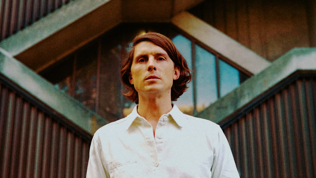 Erik Hall in white shirt photographed from below against distinctive corrugated architecture with arched structures, warm tones. Photo by Nolis Anderson.
