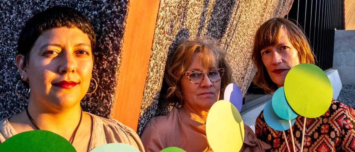 Beatriz Ortiz-Belt, Holly Tavel, and Sarah Morrison of Lost Noises Office against textured backdrop with colorful balloons. Photo by Jim Leatherman.