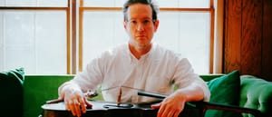 Chris Hoffman seated on a couch with a cello on his lap - Photo by Kenneth Jimenez