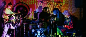 Galecstasy & Mike Watt Trio perform with psychedelic yellow-green projections, three musicians visible with electronic equipment and drums. Photo by Matthew Lawton.